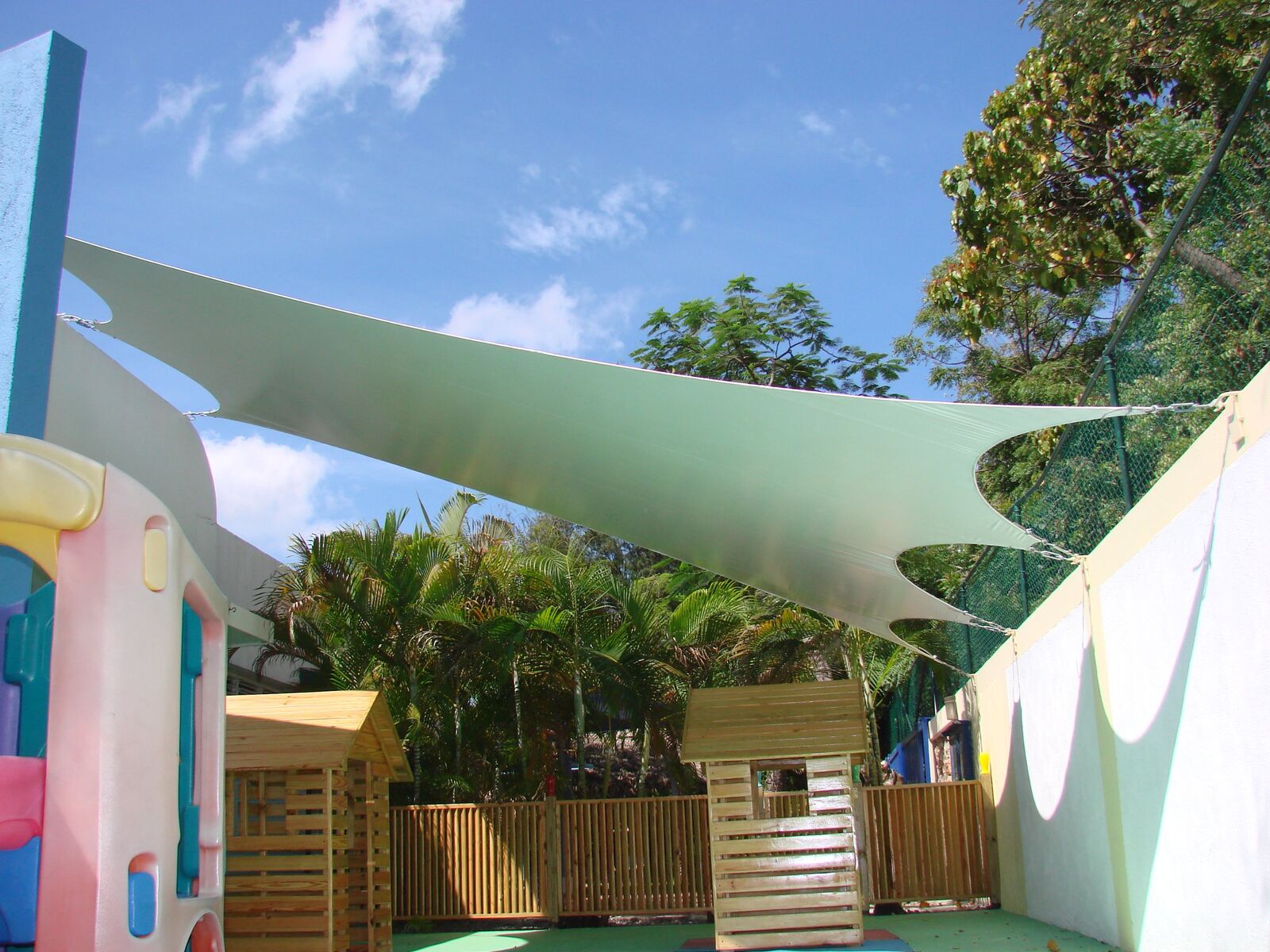 Vela tensada verde claro sobre parque infantil con casitas de madera
